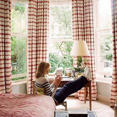 a woman sitting in a chair next to a window with red and white striped curtains