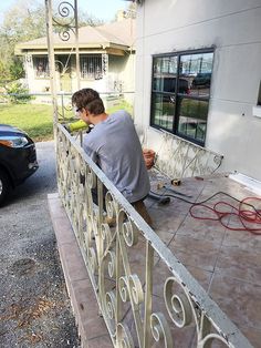 a man working on an iron railing outside his house with a car parked in the driveway behind him