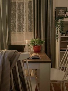 a table with a book, candle and potted plant in front of the window