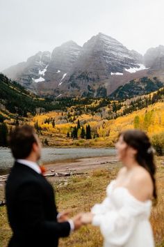 a bride and groom holding hands in front of mountains with snow on the tops during their wedding day