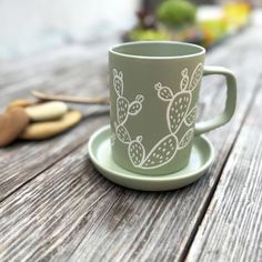 a green cup sitting on top of a wooden table next to a spoon and fork