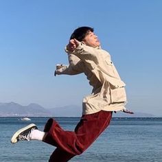 a man is jumping in the air by the water with his feet up and arms out