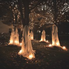 lighted ghost statues in the middle of a yard with trees and lights around them at night