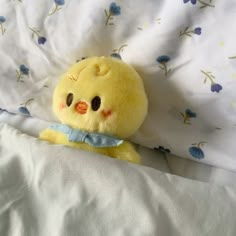 a small yellow stuffed animal laying on top of a white bed covered in blue flowers