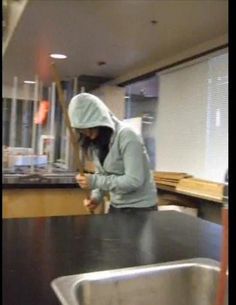 a person in a hoodie standing at a kitchen counter with a knife and fork