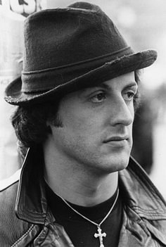 black and white photograph of a man wearing a hat with cross necklace on his neck