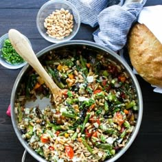 a pot filled with rice and vegetables on top of a wooden table next to bread