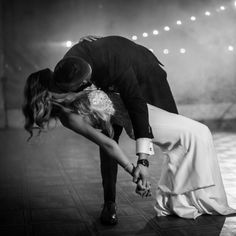 a man and woman kissing on the dance floor with lights in the back ground behind them