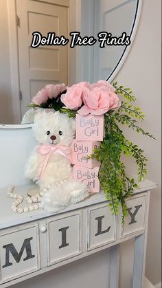 a white teddy bear sitting on top of a table with pink flowers in front of it