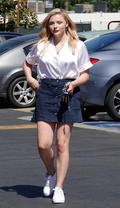 a woman is walking down the street in a skirt and white shirt with her hand on her hip