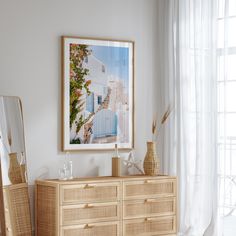 a wooden dresser sitting in front of a window next to a large mirror and vase