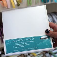 a hand holding a white paper sleeve in front of a store display shelf filled with different colored papers