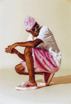 a man with pink hair and sunglasses sitting on a skateboard in front of a white background