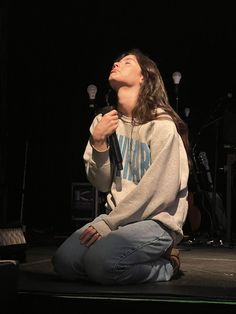 a woman sitting on the ground in front of a microphone with her eyes closed and mouth open