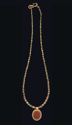 A ROMAN GOLD AND AGATE PENDANT ON A GOLD, CARNELIAN AND TURQUOISE BEAD NECKLACE CIRCA 1ST CENTURY A.D. The oval box bezel of gold sheet with a wide plain flange, the ribbed suspension loop with a single granule at the join, set with a bevelled oval agate, layered brown on white, strung as a pendant on a necklace composed of carnelian, turquoise and gold disk beads, graduated in size; strung with a modern S-hook closure 18½ in. (47 cm.) long Roman Necklace, Ancient Necklace