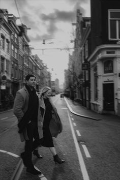 a man and woman are walking down the street in black and white, with buildings on either side