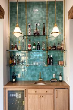 a kitchen with green tiled walls and wooden cabinetry next to a wine rack filled with bottles