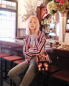 a blonde woman sitting on top of a wooden bar next to a vase filled with flowers