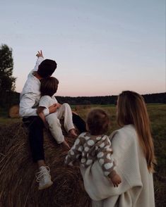 three people sitting on hay bales with one person reaching up to grab something from the other