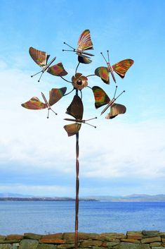 a metal sculpture with many butterflies on it's head and wings, in front of a body of water