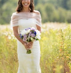 a woman in a white dress is holding a bouquet and smiling at the camera while standing in a field