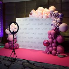 a pink and white backdrop with balloons on the floor next to a camera set up in front of it