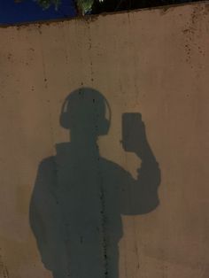 a shadow of a man holding a cell phone in front of a wall with a tree