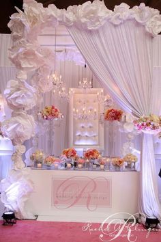 a wedding ceremony setup with flowers and chandeliers on the wall, draped in white draping