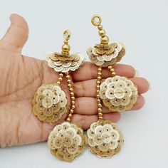 the hand is holding three gold earrings with filigrees and beads on them