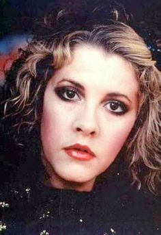 a close up of a person with curly hair and black eyeshadow, wearing an evening dress