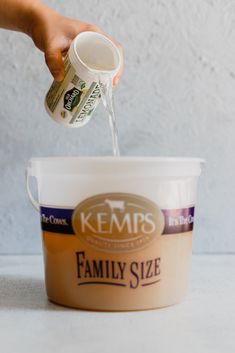 a person pouring milk into a bucket on top of a white table with the words kemp's family size written on it