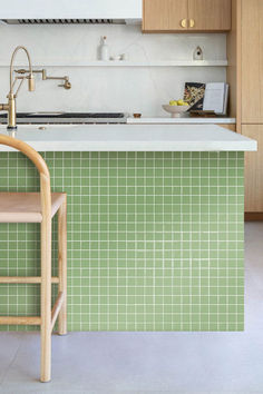 a kitchen with green tiles on the wall and wooden cabinets, along with a bar stool