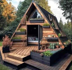 a small wooden cabin in the woods with plants and potted plants on the deck