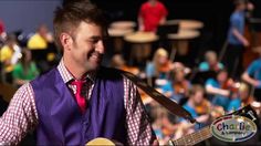 a man wearing a purple vest and red tie holding a guitar in front of an audience