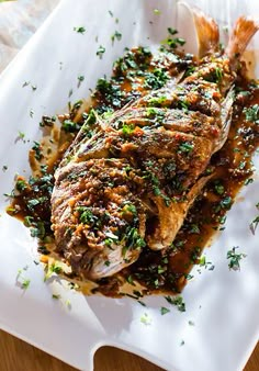 a white plate topped with fish covered in sauce and garnished with parsley