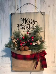 a merry christmas sign hanging on the side of a wall with pine cones and berries