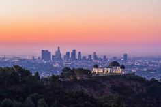 the city skyline is seen at sunset from atop a hill