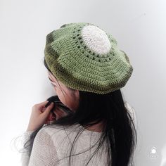 a woman wearing a green crocheted hat while talking on her cell phone in front of a white wall