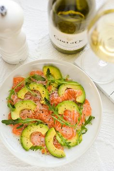 a white plate topped with salmon and cucumbers next to a glass of wine