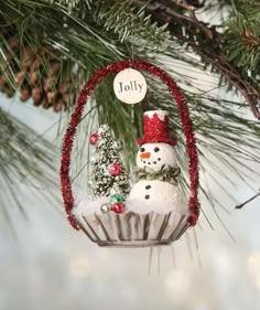 a christmas ornament hanging from a pine tree with a snowman on it