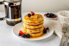 a stack of pancakes with syrup and berries on a plate next to a coffee pot