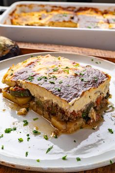 a white plate topped with lasagna covered in sauce and toppings next to a casserole dish