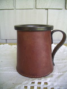 a brown leather mug sitting on top of a white table cloth next to a wooden door