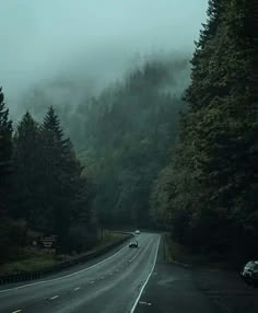 a car driving down a road in the middle of some foggy trees and hills