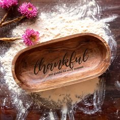 a wooden bowl filled with flour next to pink flowers on top of a table covered in powder