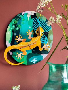 a paper plate with a yellow gecko on it next to a vase filled with flowers