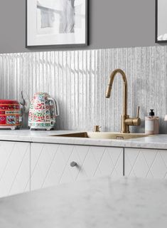 a kitchen with white cabinets and marble counter tops, two pictures on the wall above the sink