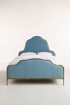 a blue bed with white sheets and gold trimmings on it's headboard