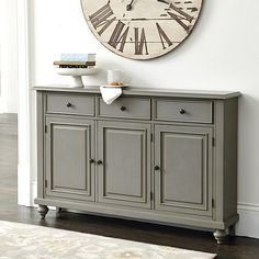 a large clock mounted to the side of a wall above a gray buffet server cabinet