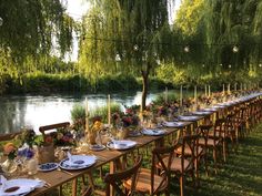 a long table is set up with plates and place settings for dinner by the river